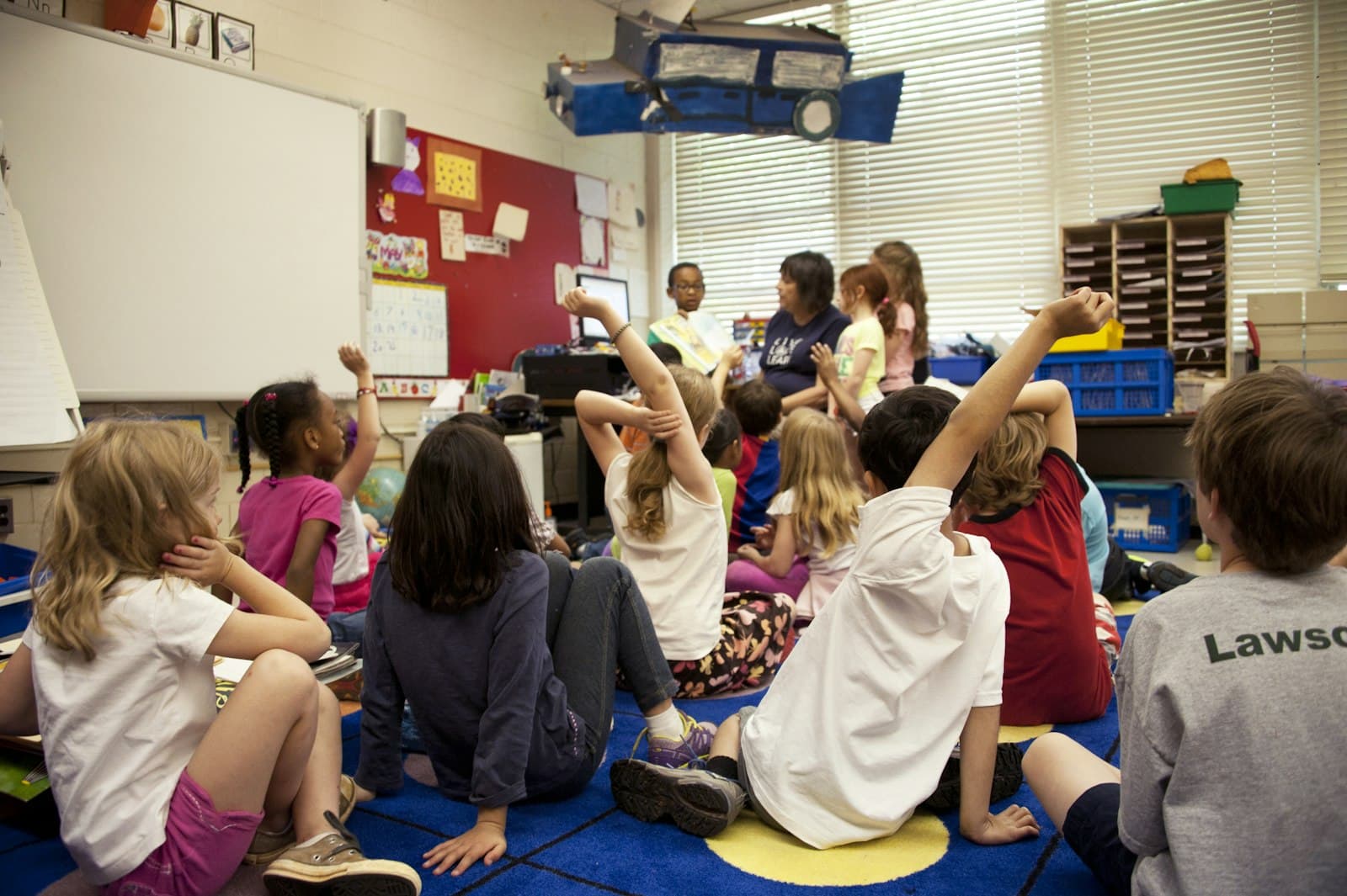 Pre-K children sitting on a carpet with hands raised during circle time