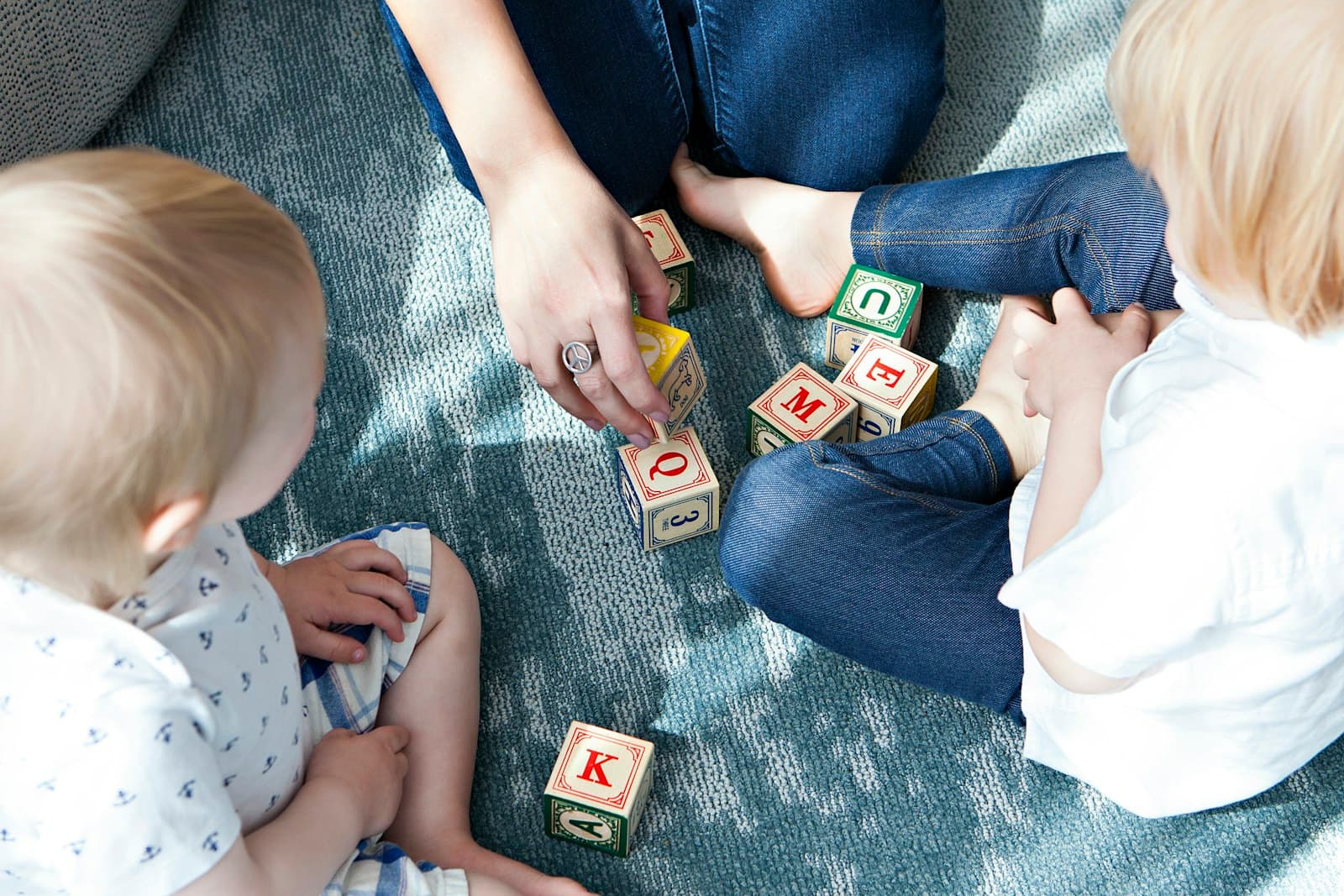 Two toddlers playing with alphabet blocks on a rug